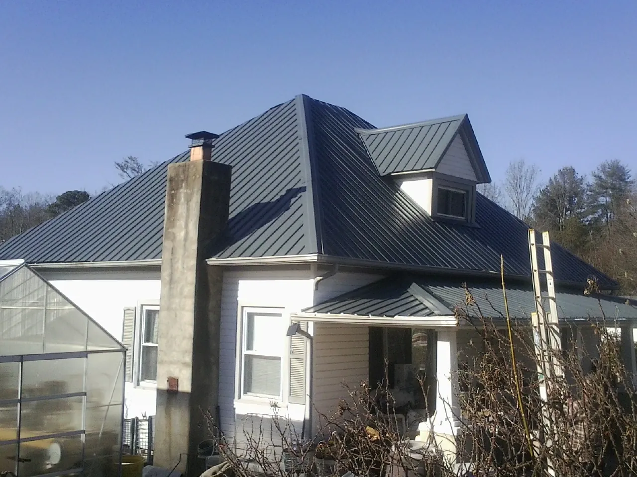 Dark blue standing seam metal roof on a white farmhouse with dormer — Slate & Tile Roof Repair by Roofing Brothers in Mount Clemens