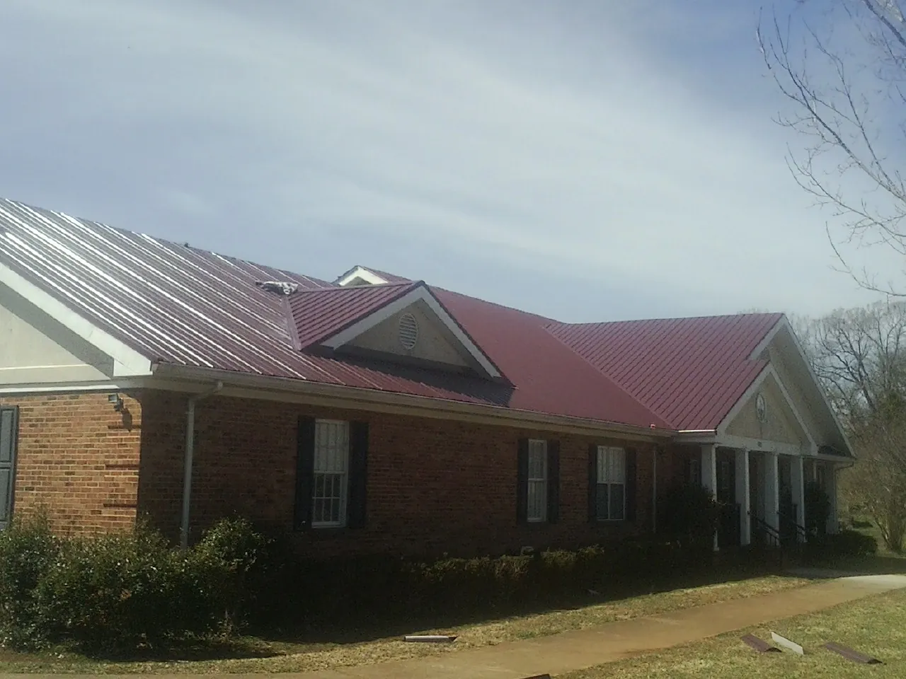 Red metal roof with gabled entries on a long brick building, from a Hail Damage Roof Repair job in Mount Clemens