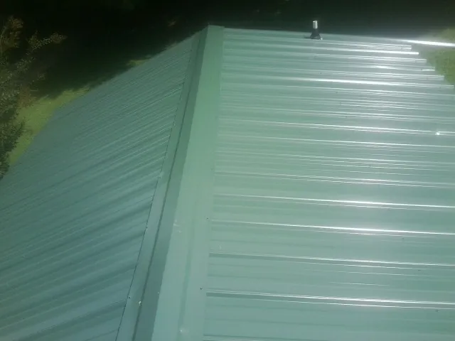 New green metal panels meeting at the ridge of a roof — Flat Roof Repair work by our crew in Mount Clemens