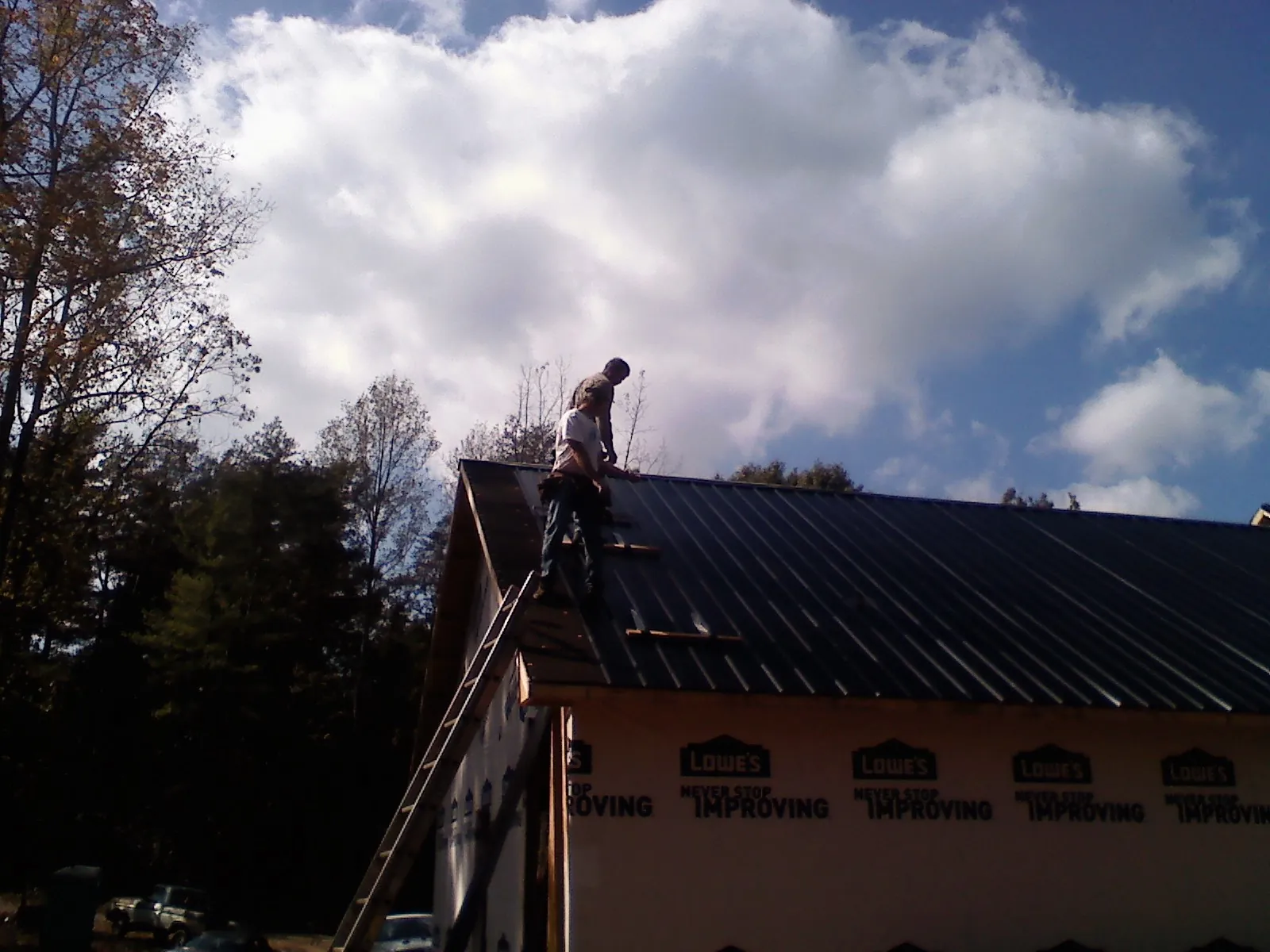 Roofer fastening dark metal panels high against a cloudy sky in Mount Clemens