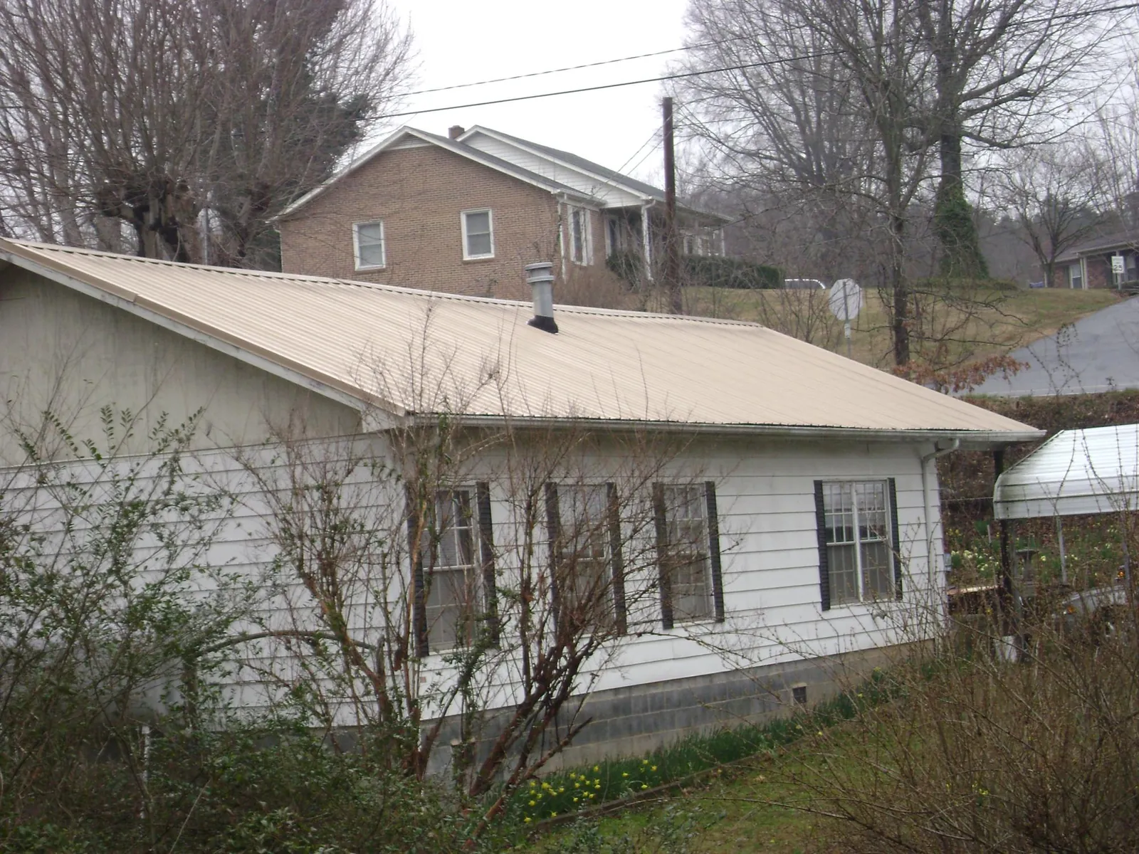 Tan metal roof on a white sided house set into a hillside — Commercial Roofing by Roofing Brothers in Mount Clemens